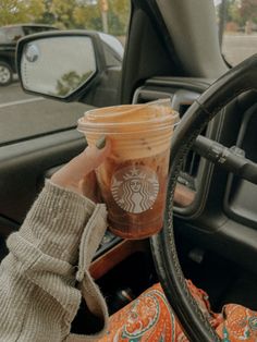 a woman holding up a cup of coffee in her hand while sitting in the driver's seat of a car