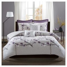 a bed with purple and white comforters in front of a window on a hardwood floor