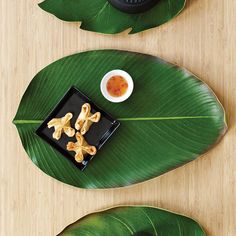 a black plate topped with cookies next to a bowl of sauce on top of a green leaf