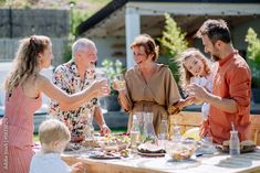 a group of people standing around a wooden table with food on it and wine glasses in their hands