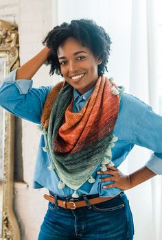 a woman is smiling and wearing a multicolored knitted scarf around her neck