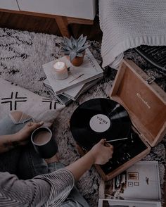 a person sitting on the floor with a record player and coffee cup in front of them