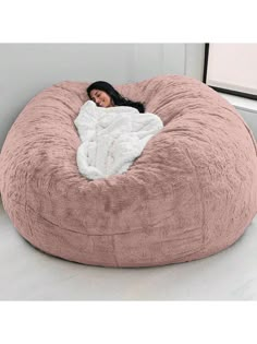 a woman laying in a large pink bean bag chair with a white blanket on it