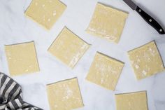 several square pieces of dough on a white counter top next to a knife and striped napkin