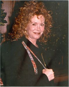 a woman with curly hair holding scissors in her right hand and smiling at the camera