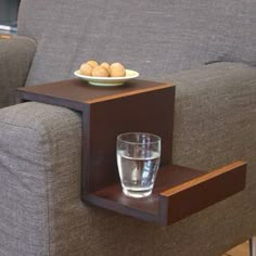 a glass sitting on top of a wooden table next to a gray couch with a bowl of food on it