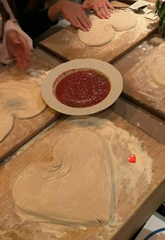 two women making heart shaped pizzas on wooden boards with red sauce in the middle