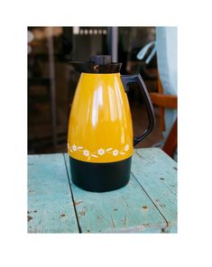 a yellow and black coffee pot sitting on top of a wooden table