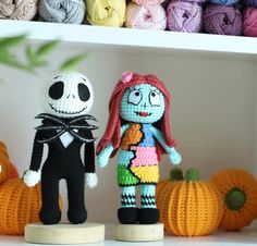 two crocheted dolls standing next to each other in front of yarn balls and pumpkins