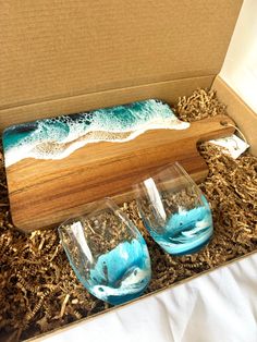 two wine glasses sitting in a box next to an empty container with the ocean painted on it