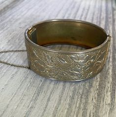 Add a touch of vintage elegance to your outfit with this beautiful Vintage Brass Hinged Bangle. The bracelet features a classic nouveau-style design with delicate floral etching, all in a stunning gold color. Approximately 1 inch tall About 2.5 inches wide Comes with original safety chain This hinged bangle is meticulously crafted and perfect for wearing alone as a statement piece or pairing with your favorite accessories. Don't miss out on adding this charming vintage piece to your collection! Adjustable Silver Jewelry For Vintage Events, Antique Adjustable Bracelets For Wedding, Antique Adjustable Wedding Bracelets, Vintage Bangle Bracelets For Wedding, Vintage Bangle Jewelry For Wedding, Vintage Charm Bracelets For Wedding, Vintage Bangle For Wedding, Antique Adjustable Cuff Bracelet For Formal Occasions, Elegant Antique Gold Bracelet Jewelry