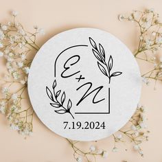 a round wedding sticker with the initials and date printed on it next to flowers