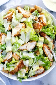 a white bowl filled with lettuce and chicken next to a fork on top of a table