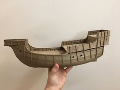 a paper model of a boat being held up by a person's hand in front of a white wall