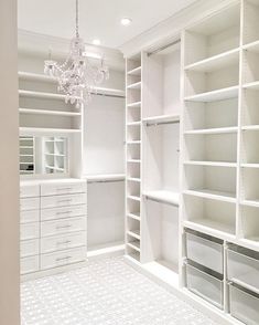 a white closet with lots of shelves and drawers on the bottom shelf, in front of a chandelier