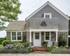 a gray house with white trim and flowers around the front door is surrounded by greenery