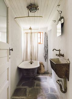 an old fashioned bathtub and sink in a bathroom with white walls, stone flooring and exposed lighting