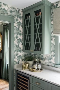 a kitchen with green cabinets and white counter tops in front of a wallpapered wall