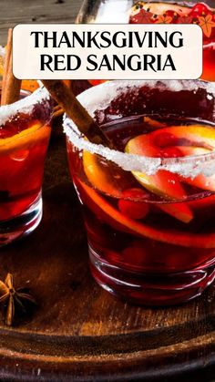 two glasses filled with red sangria sitting on top of a wooden table next to cinnamon sticks