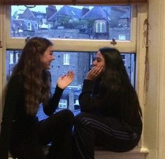 two women sitting on a window sill talking