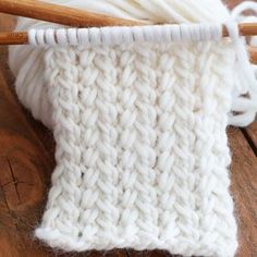 a close up of a white knitted object on a wooden table with knitting needles