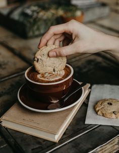 a person holding a cookie over a cup of chocolate chip cookies on top of a wooden table