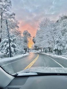 the sun is setting on a snowy road with trees and snow - covered roads in the foreground