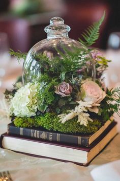 an arrangement of flowers and greenery under a clochet on top of a book