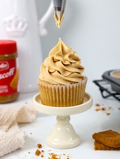 a cupcake being dunked with frosting on a white cake stand next to cookies