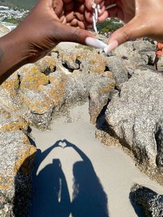 two people holding out their hands over some rocks with the shadow of one person's hand