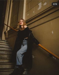 a woman is sitting on the steps with her hand in her pocket and looking up