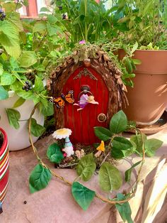 a red fairy door surrounded by potted plants and other decorations on a table outside