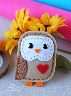 a felt owl with a heart on it's chest and sunflowers in the background