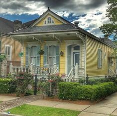 a yellow house with blue shutters and white trim on the front porch is surrounded by greenery