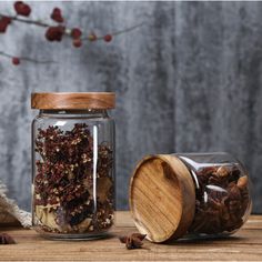 two glass jars filled with different types of spices sitting on top of a wooden table