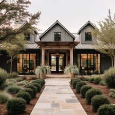 a large house with lots of windows and plants in the front yard, along with a stone walkway leading to it