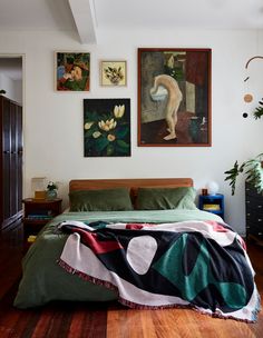 there is a bed with green sheets and paintings on the wall