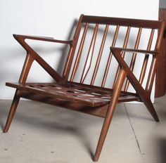 a wooden chair sitting on top of a cement floor next to a white wall,