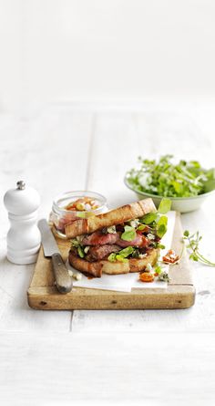 a sandwich with meat, lettuce and tomatoes on a cutting board