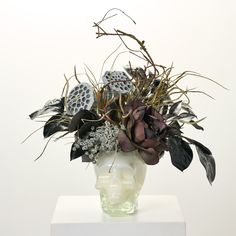 a skull vase with flowers in it sitting on a white pedestal against a white wall