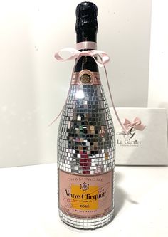 a bottle of wine with a pink ribbon around it and a gift box in the background