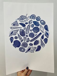 a hand holding up a blue and white print with sea shells on the inside of it