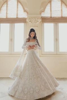 a woman in a white wedding dress standing next to two windows with large arched windows