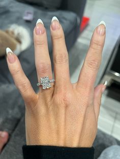 a woman's hand with a diamond ring on top of her left hand, in front of a couch