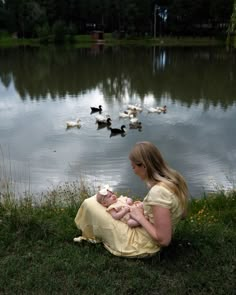 a woman is holding a baby while ducks are swimming in the water behind her,