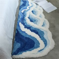 a blue and white rug sitting on top of a bed next to an open book