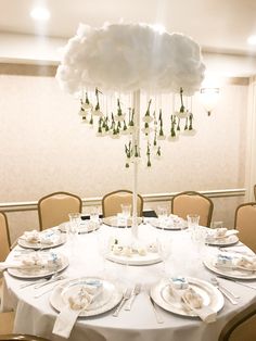 a round table with plates and place settings under a cloud shaped chandelier