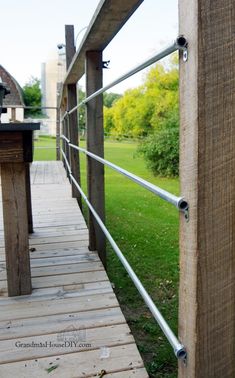 a close up of a wooden walkway with metal bars on the end and grass in the background