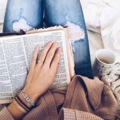 a woman reading a book with her hands resting on top of the book and holding a coffee mug