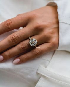 a woman's hand with a diamond ring on her left hand, wearing a white shirt